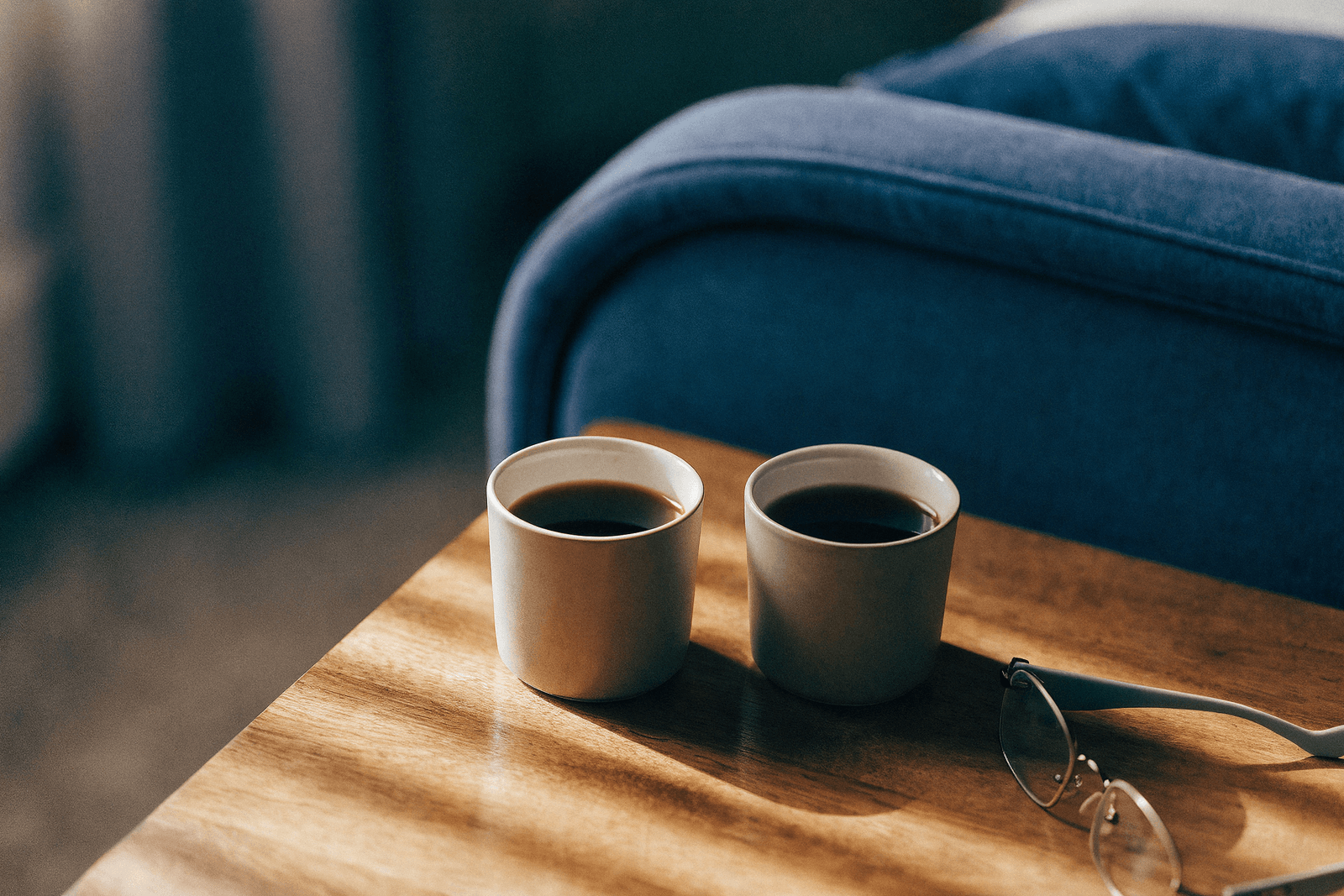 Duas xícaras de café sobre uma mesa de cabeceira ao lado de óculos de leitura na luz da manhã · saúde do homem e a vida a dois