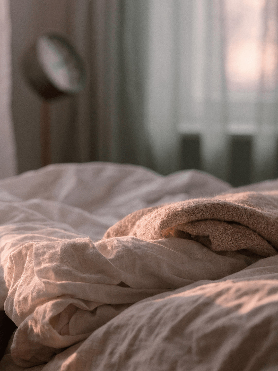 Cabeceira ao amanhecer com ventilador, copo de água e lençóis amassados · noites de calor e sono interrompido na menopausa